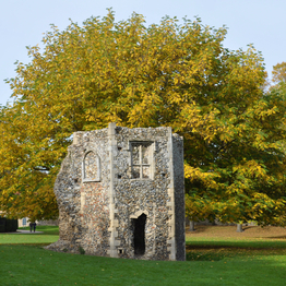 Remains of a flint building, with an early autumn tree behind it within a park.